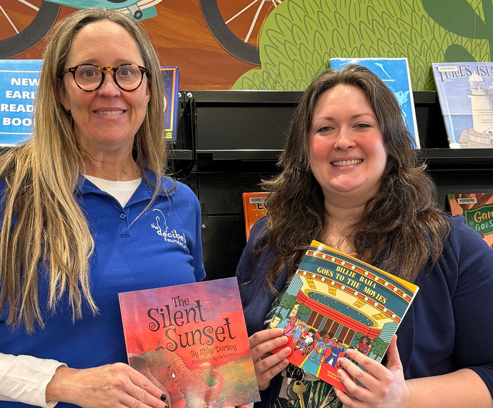 Two librarians with books donated by Decibels Foundation